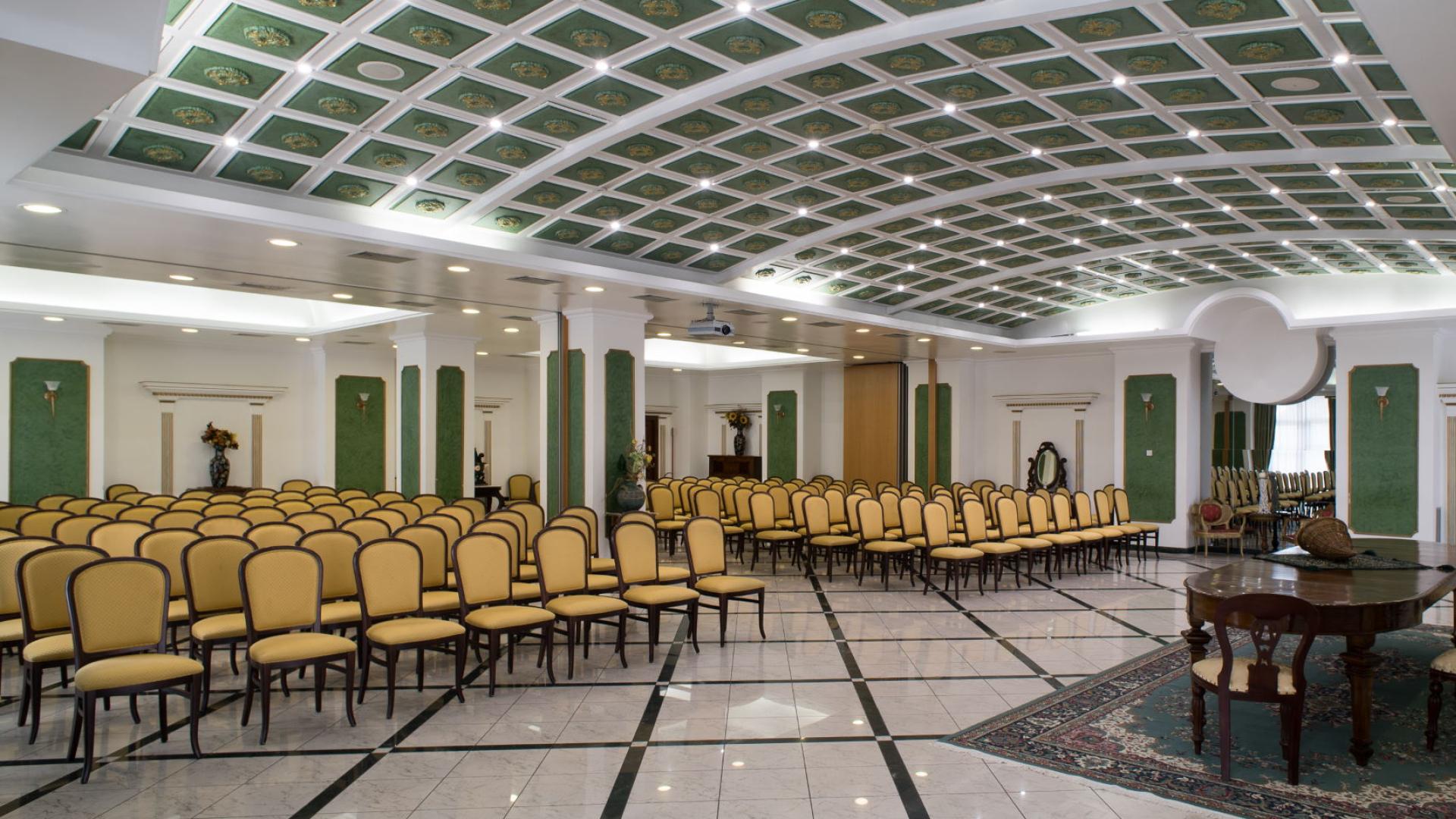 Sala conferenze elegante con sedie gialle e soffitto decorato in verde.