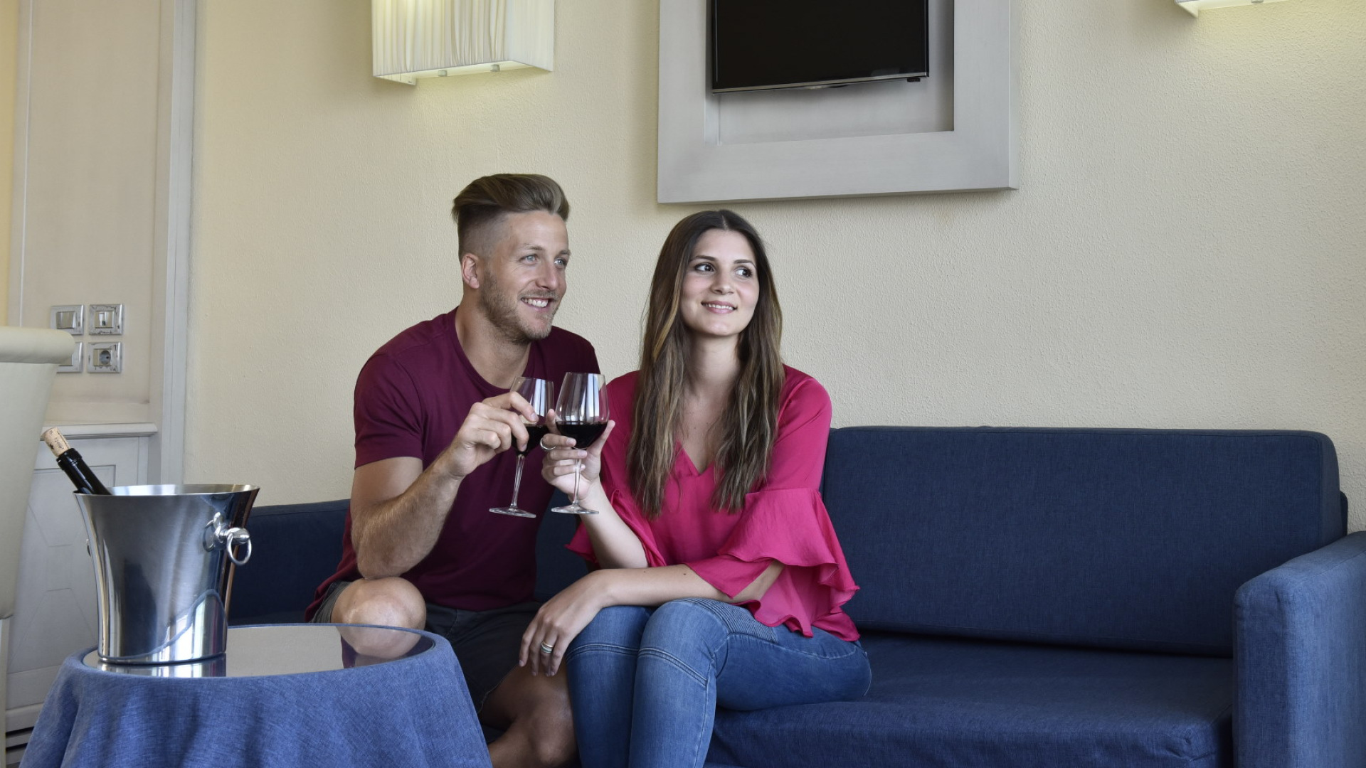 Coppia felice brinda con vino rosso su un divano blu in soggiorno elegante.