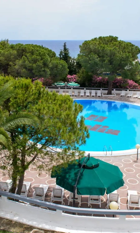 Piscina circondata da lettini, vista mare, alberi e ombrelloni verdi.